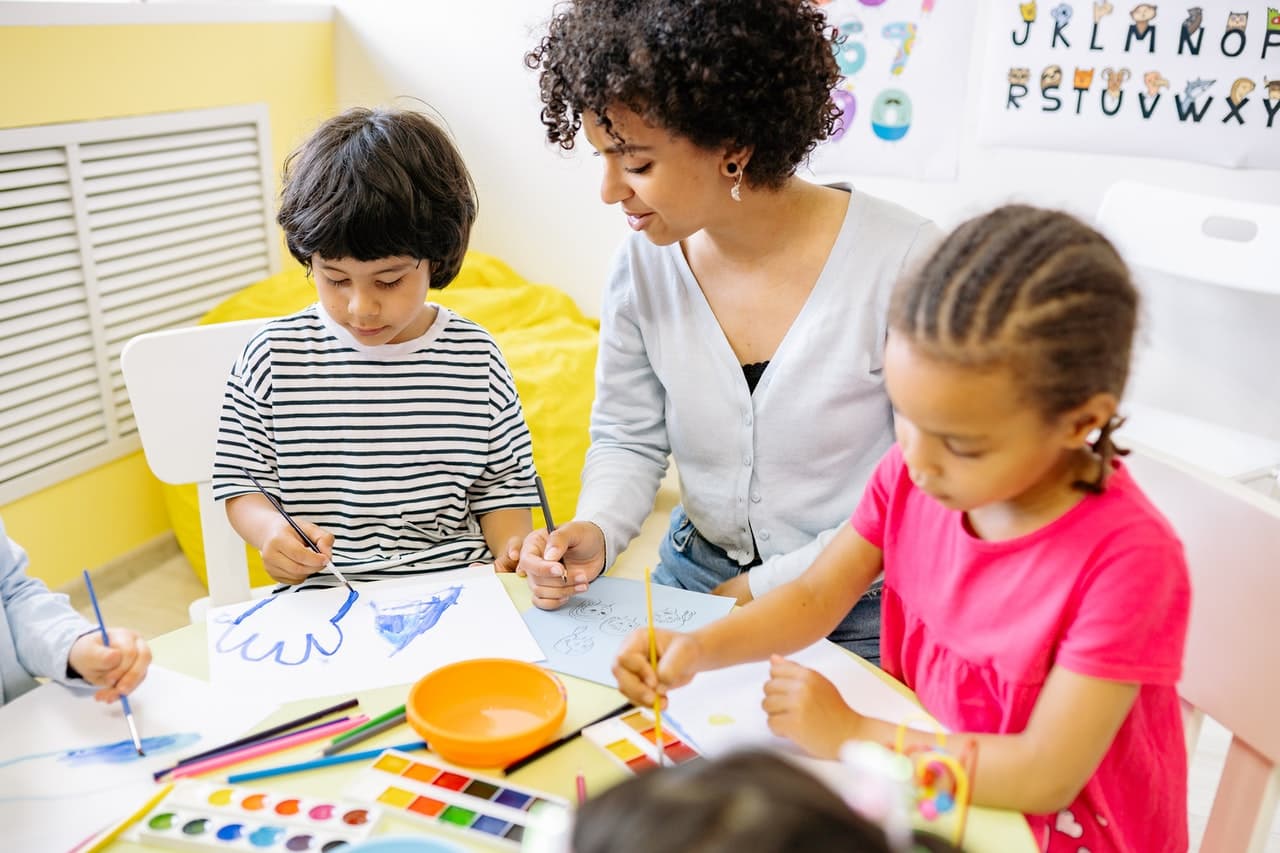 Children painting with watercolours beside an educator